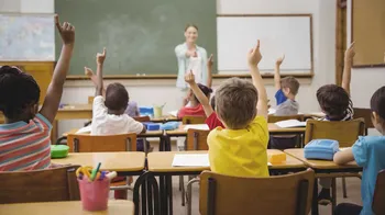 Lehrkraft in vor sich meldenden Schüler*innen
