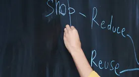 Hand schreibt auf eine Tafel: Stop, reduce, reuse 